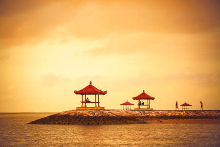 Gazebos on tropical beach during sunrise on Bali island, Sanur, Indonesia. People greet the dawn.の写真素材