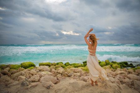 A beautiful girl in a white dress stands on the shore of the Cancun beach. Caribbean Sea.の写真素材