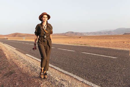 A beautiful girl in a hat is walking near the road in the desert. Moroccoの写真素材