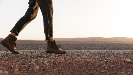 A girl in boots walks along a road made of small stones. Part of the body - legs