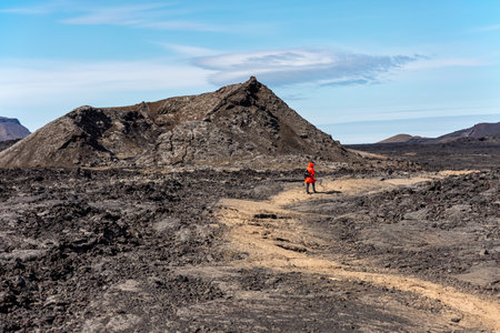 A tourist woman in a red jacket walks along a volcanic plateau in Iceland.の写真素材