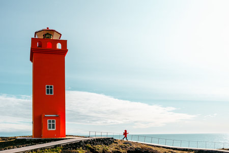Svortuloft Lighthouse in Snaefellsnes National Park, Iceland. A tourist woman in a red jacket walks...