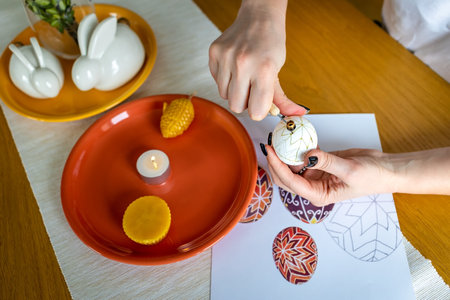 A woman decorating easter eggs with a candle on the table.