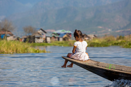 A little Asian girl sits on the edge of a boat and looks at the lakeの写真素材