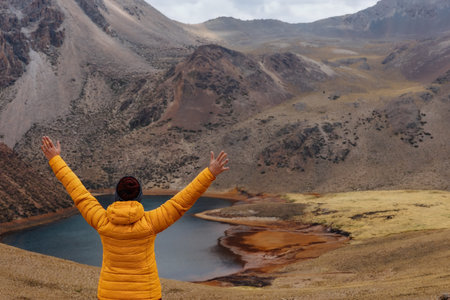 A girl in a yellow jacket with raised hands looks at the mountains and the lagoon. Uyuni .Tomave....