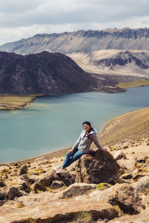 A woman tourist sits on a stone against the background of mountains and a lagoon in Bolivia .Urubamba .Uyuni .Tomave. Potosi.の写真素材