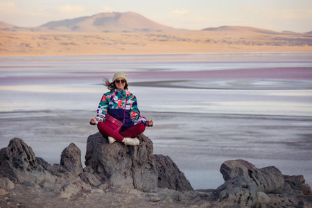 A happy girl is sitting on a large stone against the background of the Colorado lagoon. Boliviaの写真素材