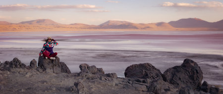 Panorama of Laguna Colorada. Bolivia. The girl is sitting on a big stone on the background of the lagoon at sunsetの写真素材