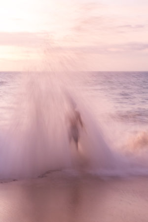 Blurred sea background at pink sunset. The silhouette of a guy is visible through a large wave that covered himの写真素材