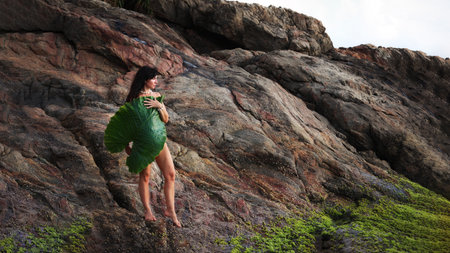A girl with a large leaf stands on a rock and looks into the distance.の写真素材