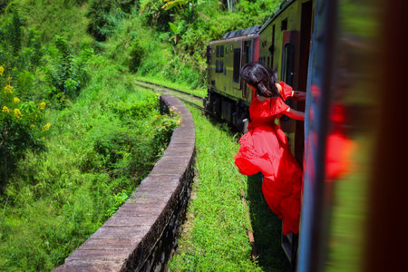 Girl in a red long dress looks out of the train. Train journey from Nuwara Eliya to Ella. Sri Lanka.の写真素材