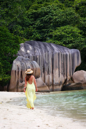 Woman in a yellow dress on a tropical beach near huge rocks in the Seychellesの写真素材