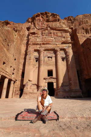 Woman resting on a traditional rug in front of an ancient rock-cut tomb in Petra, Jordanの写真素材