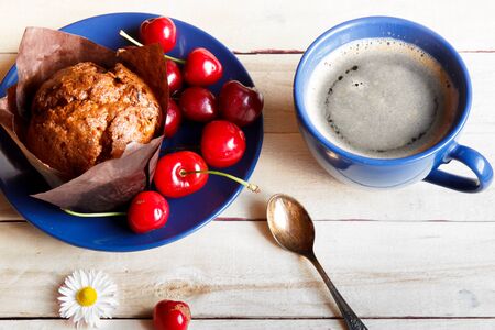 Chocolate muffin with cherries on the plate. A Cup of coffee. Blue dishware and wooden background.の写真素材