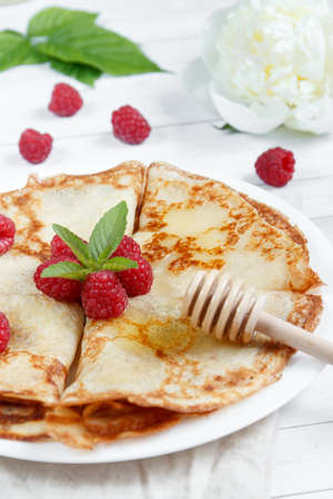 Thin pancakes with honey and raspberries on a white plate.の写真素材