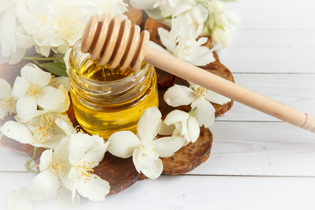 Jar and a spoon with honey on a wooden stand with Jasmine flowers,の写真素材