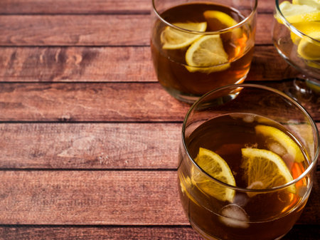 Glasses of cocktail with ice and lemon on wooden table close-up.