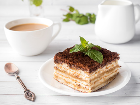 Tiramisu Dessert with Mint and Cup of Coffee on White Wooden Table.