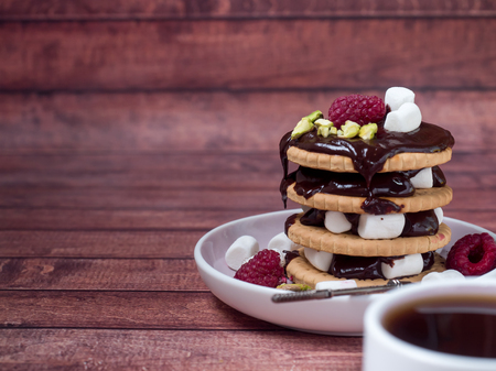 A sweet dessert of chocolate biscuit, raspberry marshmallow and a cup of coffee on dark backgroundの写真素材