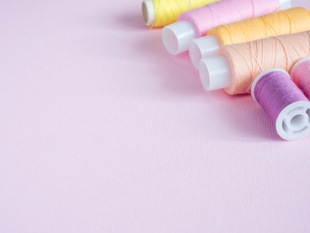 Colorful sewing buttons and thread on a pink background