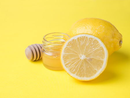 A jar of honey and fresh lemon on a bright yellow background.の写真素材