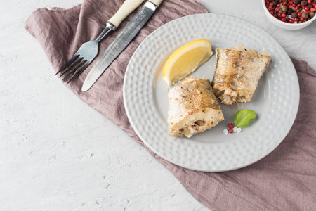 Baked Pollock fish with lemon and spices on a plate Napkin on the table.