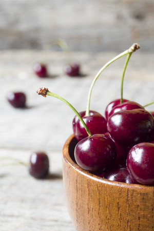 Juicy ripe cherries with sprigs in a wooden bowl on a rustic background.の写真素材