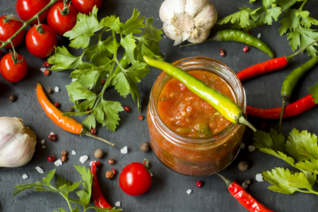 Sauce ketchup, Lecho in glass jar. Chili tomato cherry garlic and other spices on black background.の写真素材