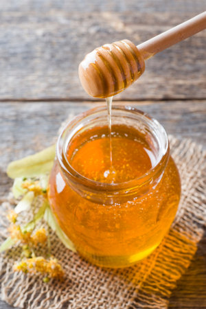 Glass jar of honey, Linden flowers on wooden background.