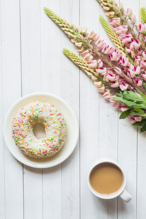 Still life with a Cup of coffee and lupine flowers donut on a light wooden tableの写真素材