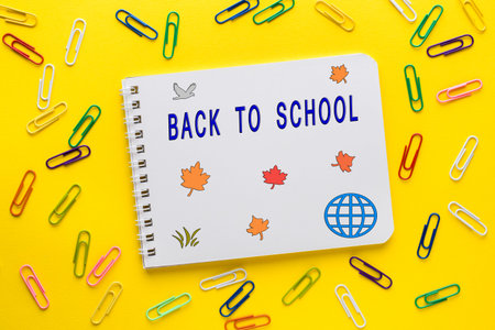 Notebook and colored paper clips on yellow background. Back to school.