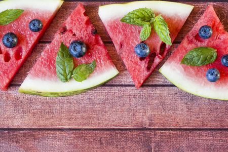 Pieces of sliced watermelon with mint and blueberries on a rustic dark background. Summer concept.の写真素材