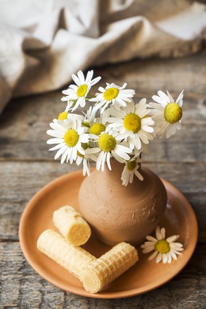 Still life of a bouquet of daisies in a vase and waffle tubes. Wooden rustic styleの写真素材