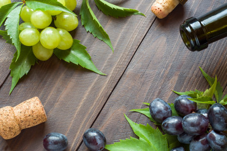 Bunch of red and white grapes, bottle of wine and cork on wooden table background with copy space.