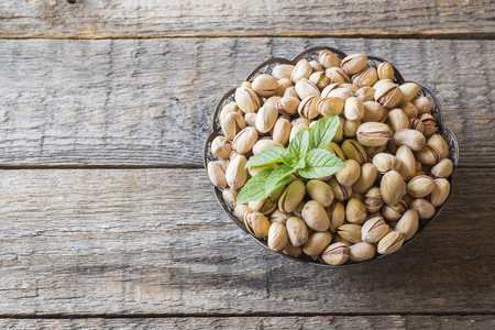 Delicious salted pistachios and fresh mint leaves on wooden backgroundの写真素材