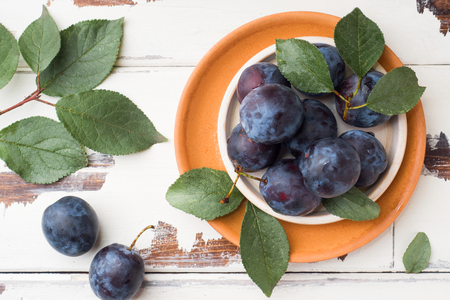 Fresh plum berries on a plate with leaves on a light tableの写真素材