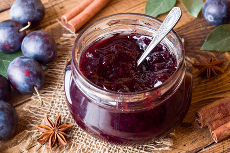 Plum jam in a glass jar. Fresh plum fruit on a wooden table