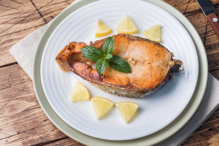 Steak baked fish salmon on a plate with lemon. Wooden table