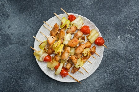 Kebab chicken, zucchini and tomatoes on skewers in a plate. Dark table. Copy spaceの写真素材