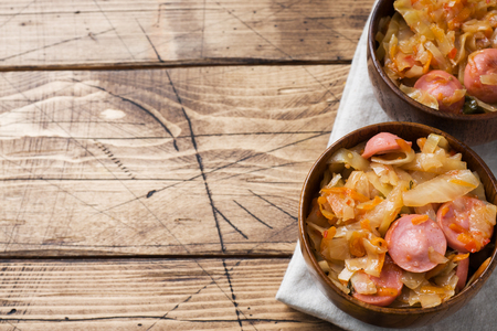 Stewed cabbage with sausages in wooden bowls on the table. Selective focusの写真素材