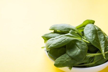 Fresh spinach leaves in a plate on a yellow backgroundの写真素材
