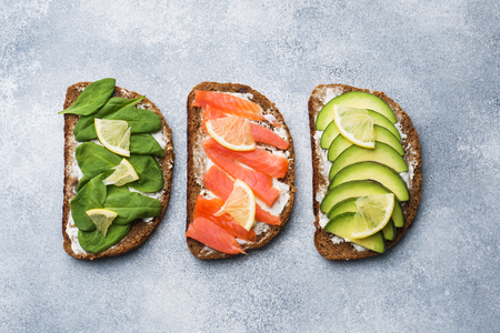 Open sandwiches with spinach and avocado salmon on a grey tableの写真素材