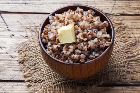 Boiled buckwheat with a piece of butter in a wooden bowl on a rustic tableの写真素材