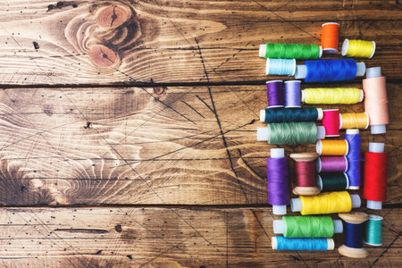 Colored spools of thread laid out in rows on wooden background. Copy space