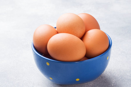 Brown raw Chicken eggs in a blue bowl on a grey background