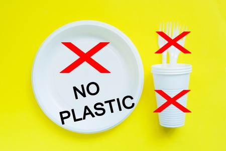 Disposable plastic tableware on bright yellow background with copy space concept of protest and the words No Plasticの写真素材