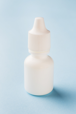 White bottle on a blue background. Round white plastic bottle for medical or cosmetic liquid, eye drops, oil. Realistic packaging layout template. Side viewの写真素材