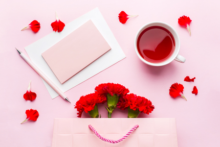 Red-pink objects. Cup of tea, carnation flowers Notepad for text on pastel pink background. Copy space. Top view Flat lay.の写真素材