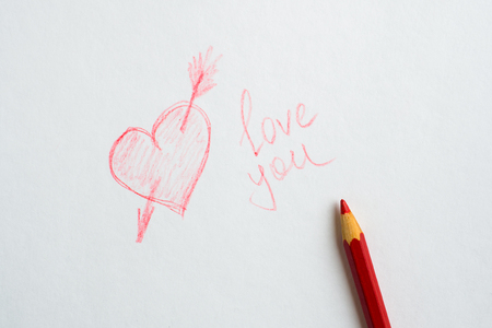 Heart drawn on paper, the inscription love you and a red pencil on white paperの写真素材