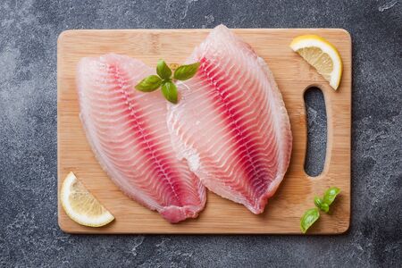 Raw fish fillet of tilapia on a cutting Board with lemon and spices. Dark table,の写真素材